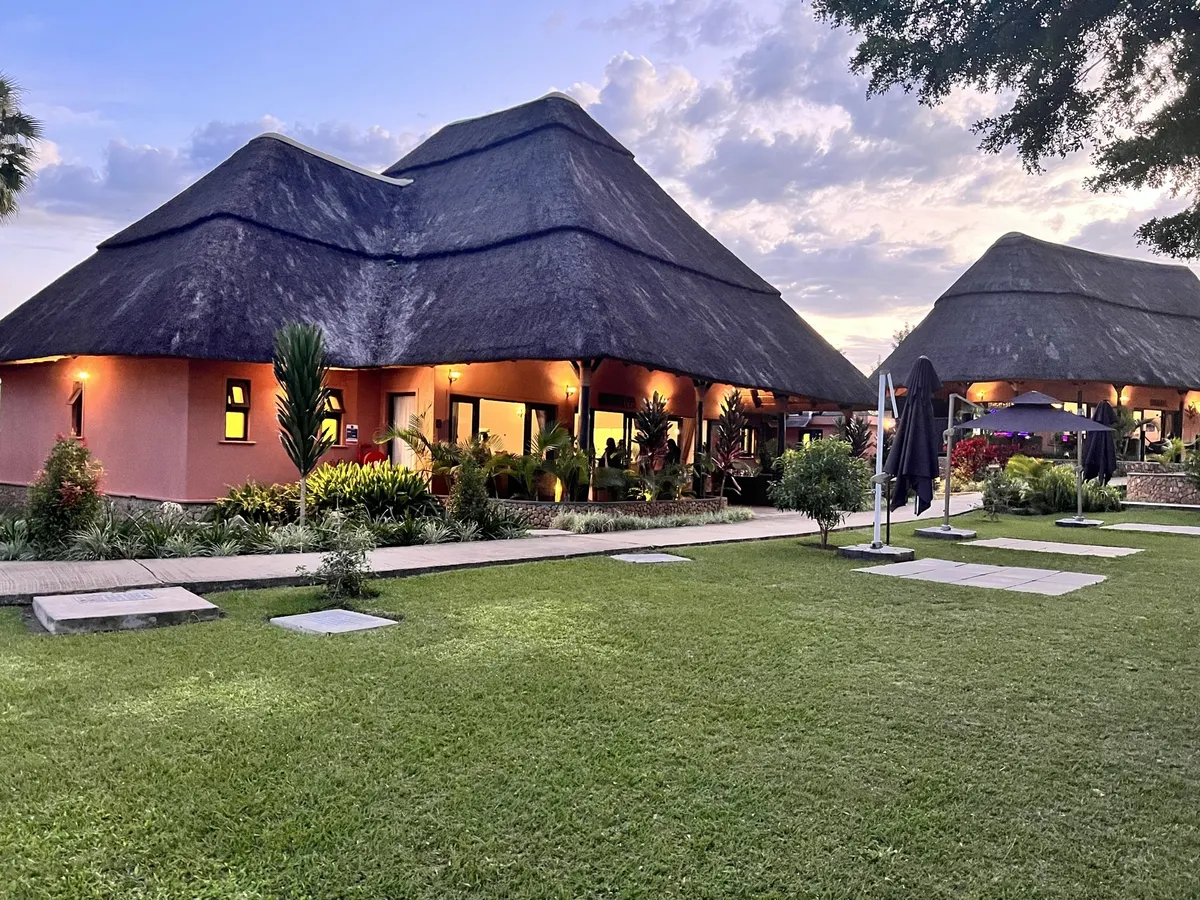 Thatched-roof cottages with lit windows on a green lawn at dusk